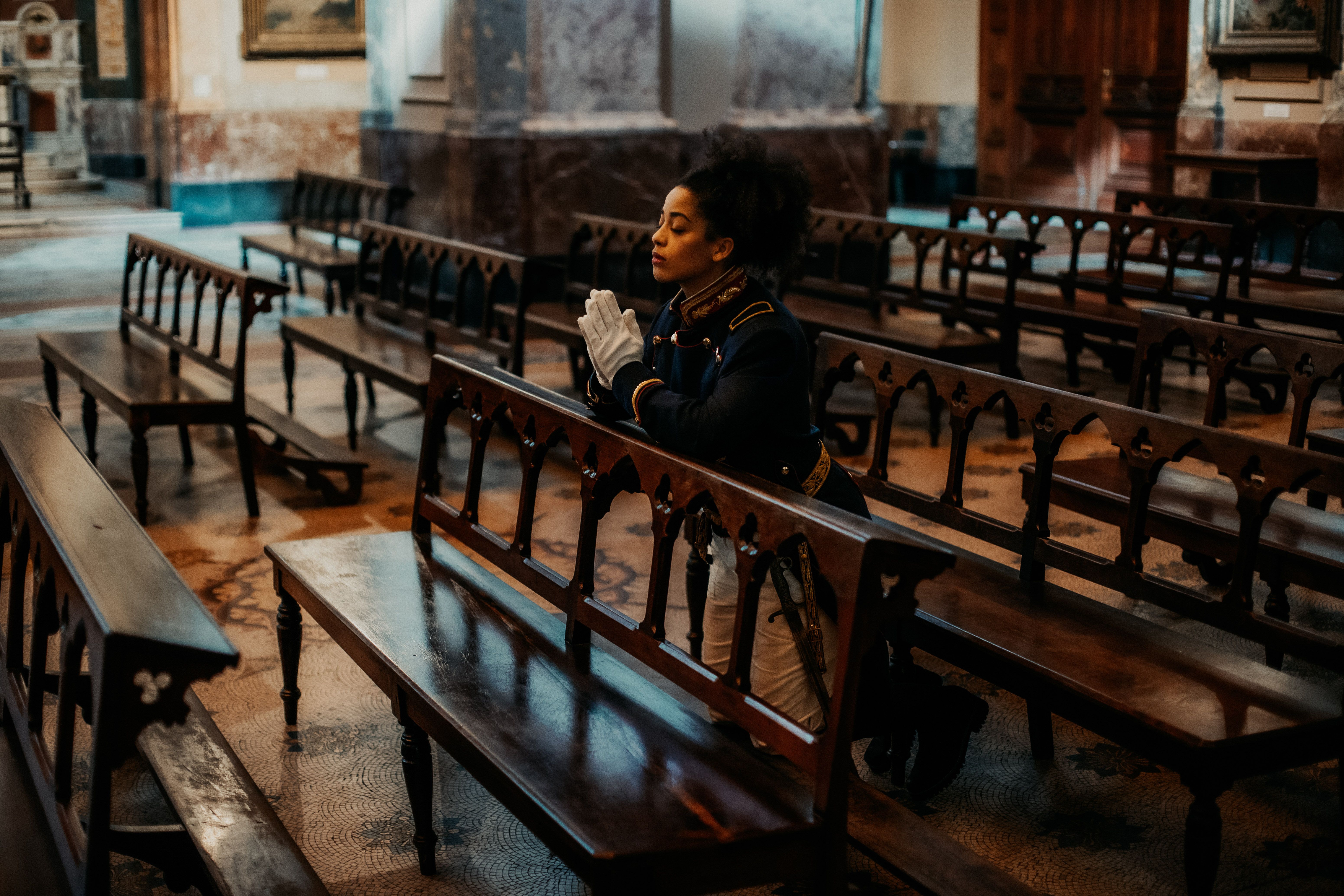 A woman in elegant attire kneels in prayer inside a historic church in Buenos Aires, Argentina.