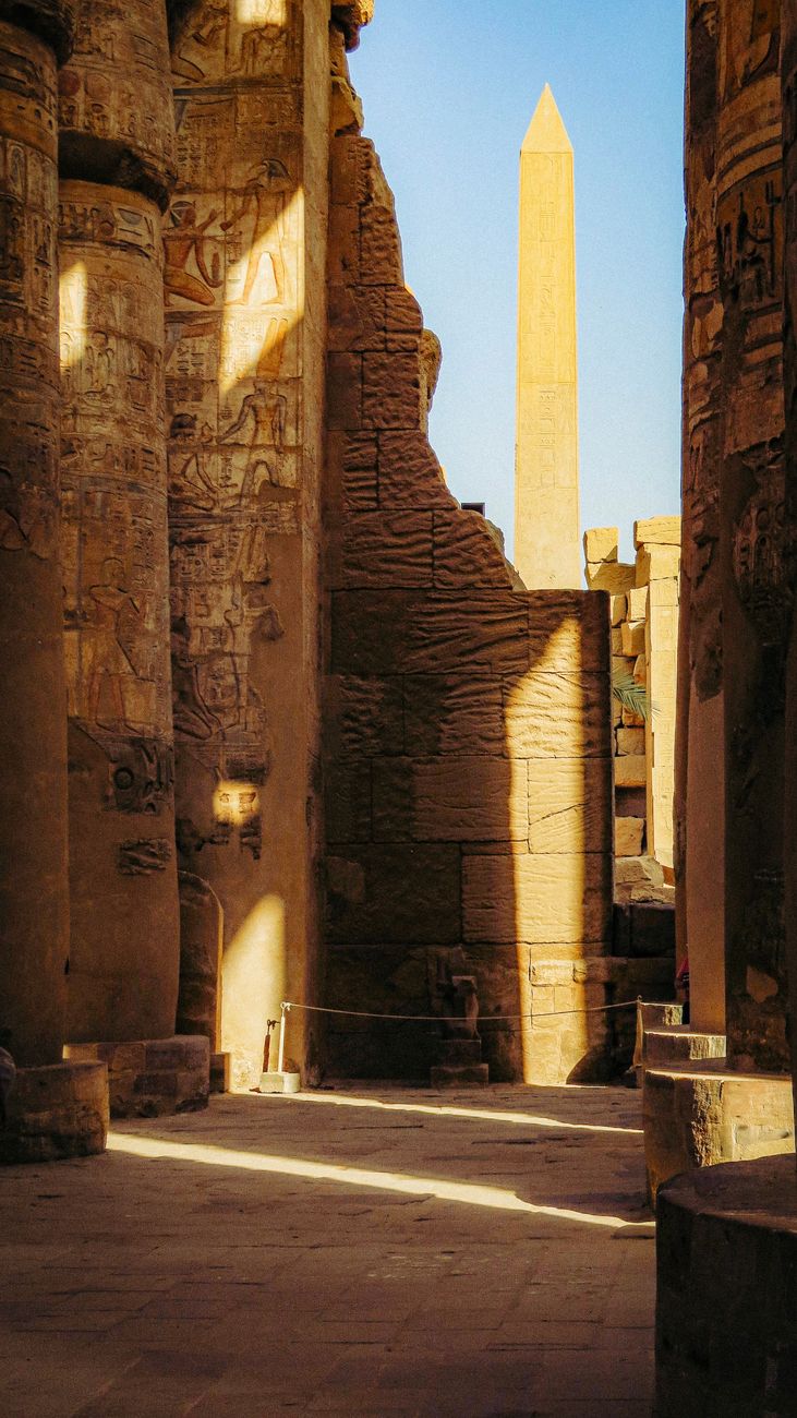 Een indrukwekkend uitzicht op een oude Egyptische tempel met gebeeldhouwde stenen pilaren en een torenhoge obelisk, badend in het warme zonlicht.