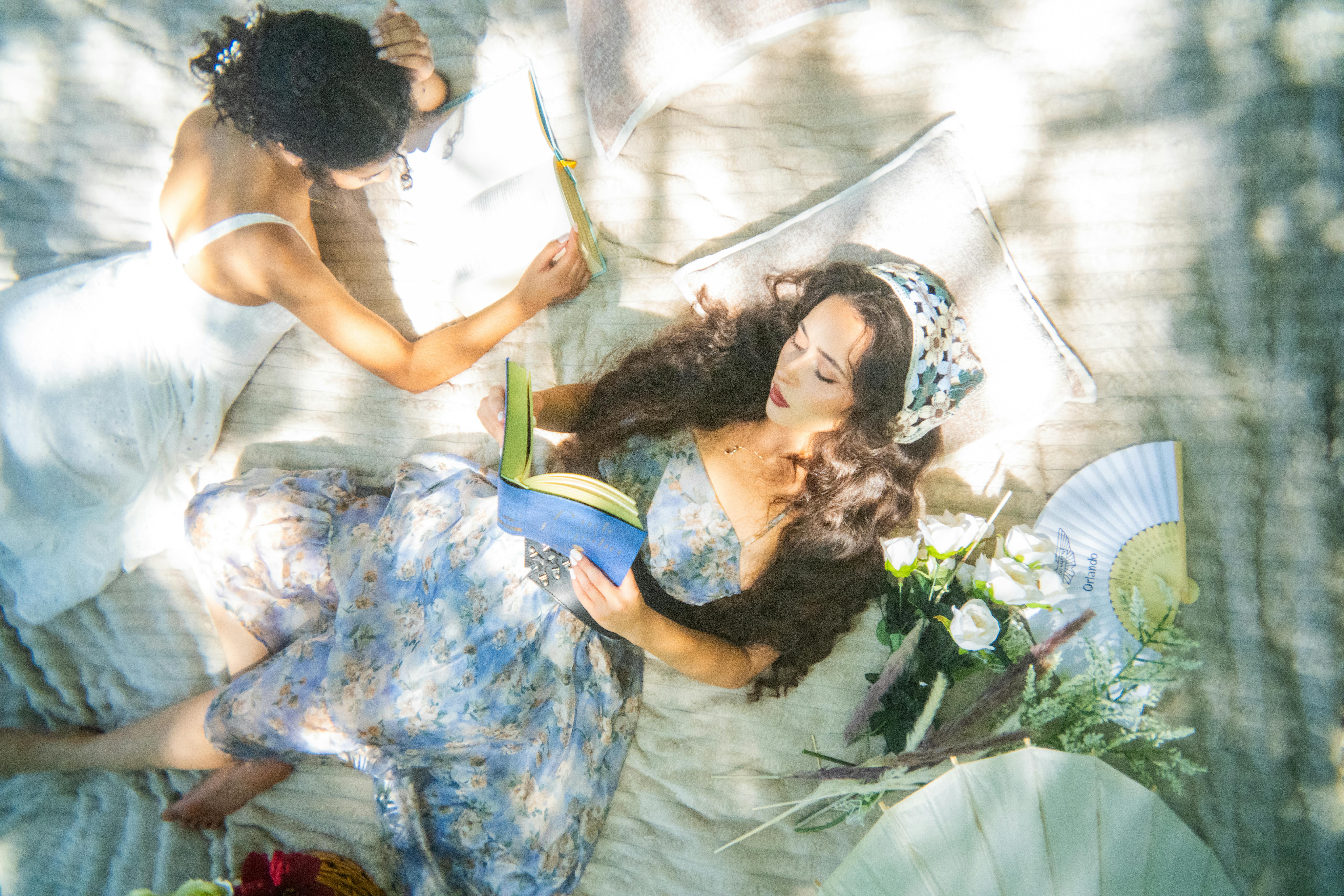 Two women enjoying a sunny day outdoors, relaxing and reading in a sunlit garden setting.