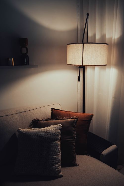 Free Elegant living room with a beige sofa, warm lighting, and brown cushion accents creating a serene ambiance. Stock Photo