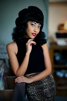 Woman with vintage hairstyle and leopard skirt poses stylishly indoors.