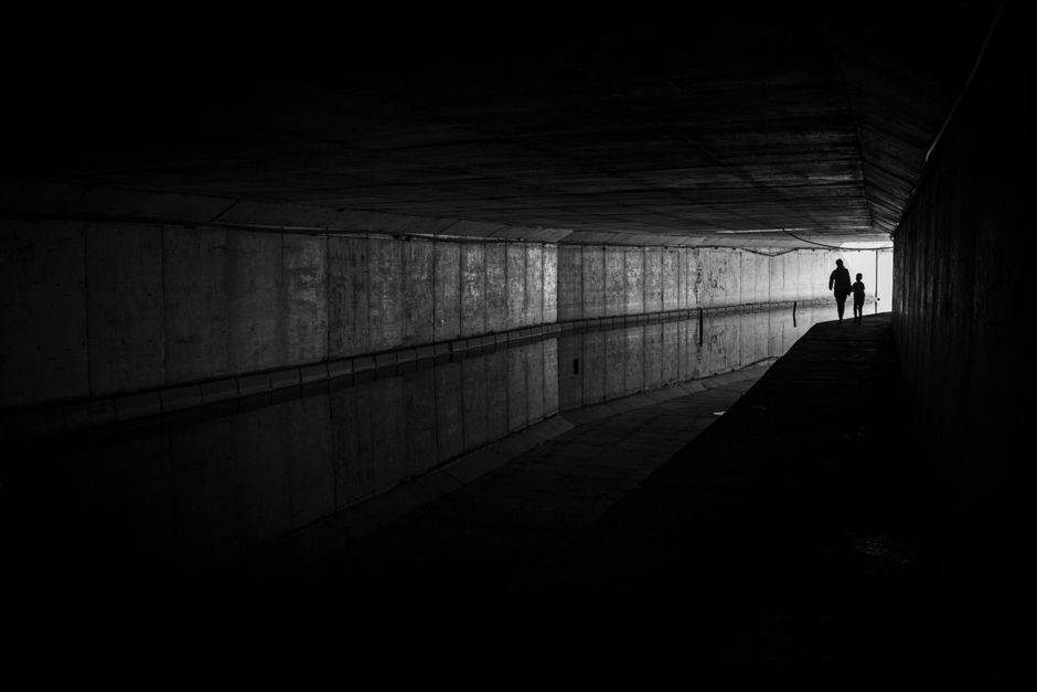 Moody black and white photo of silhouettes walking in tunnel.