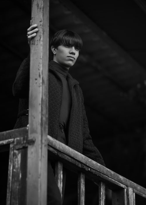 Free A striking black and white portrait of a person standing on a wooden balcony with a moody expression. Stock Photo