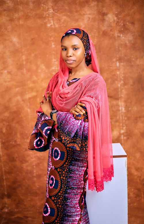 Free Portrait of a woman wearing colorful African attire and headscarf against a brown backdrop. Stock Photo