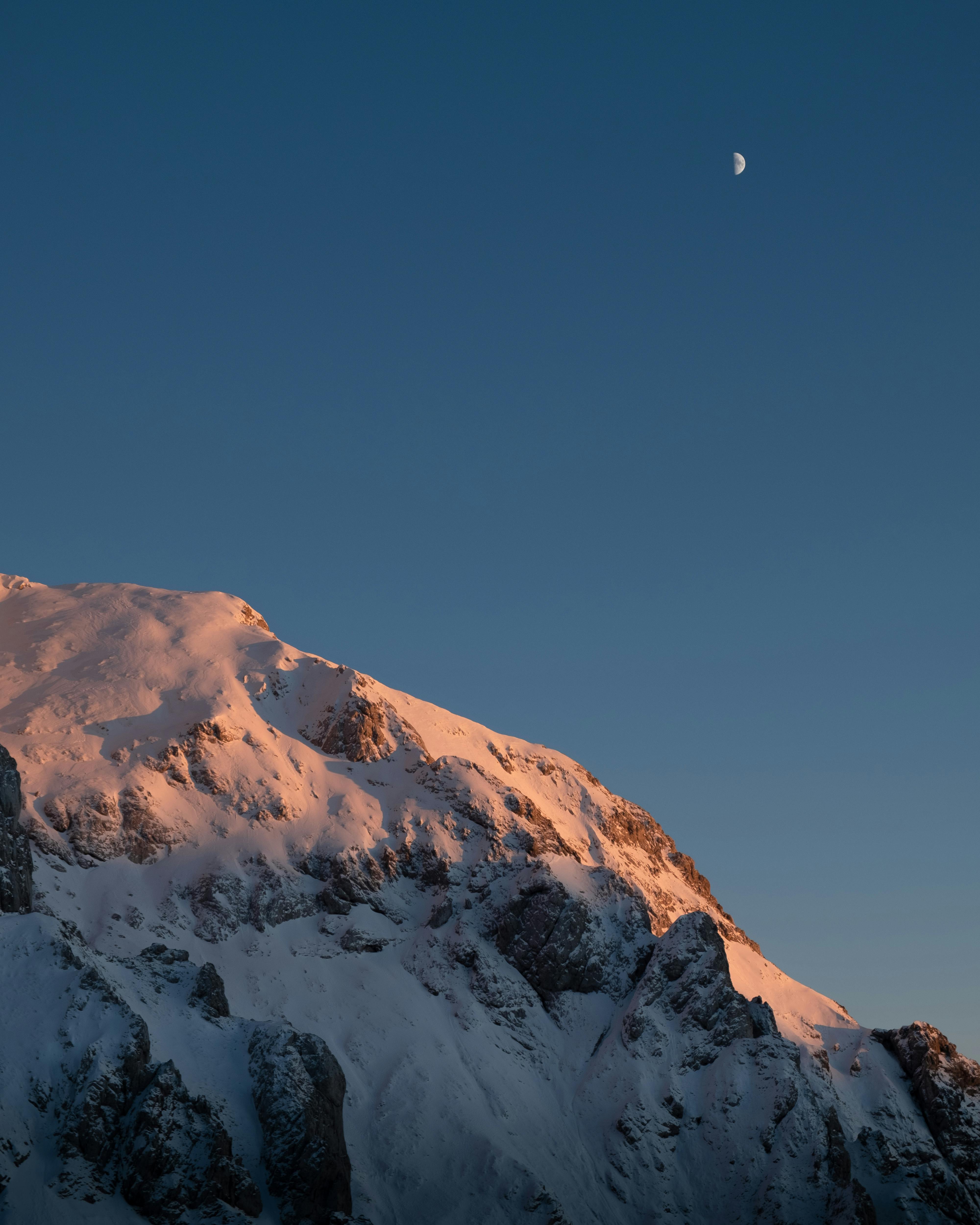 Stunning view of a snowy mountain peak at twilight with the moon in the sky, Kamnik, Slovenia.