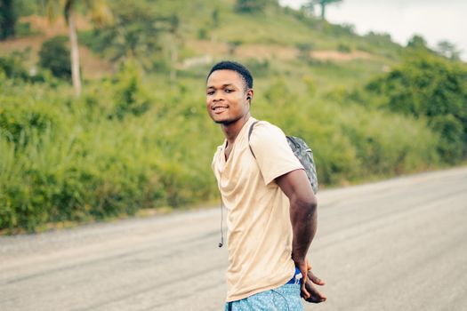A young man wearing a backpack walking on a rural road, exuding confidence and warmth.