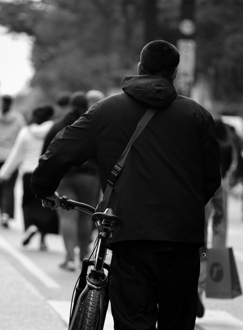 Free A black and white photo of a cyclist walking his bike through a crowded urban street. Stock Photo