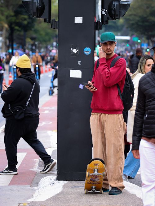 Free A young man stands with a skateboard, waiting at a busy city crosswalk. Stock Photo