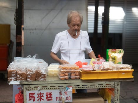 Elderly man selling traditional Asian pastries at street market stall.