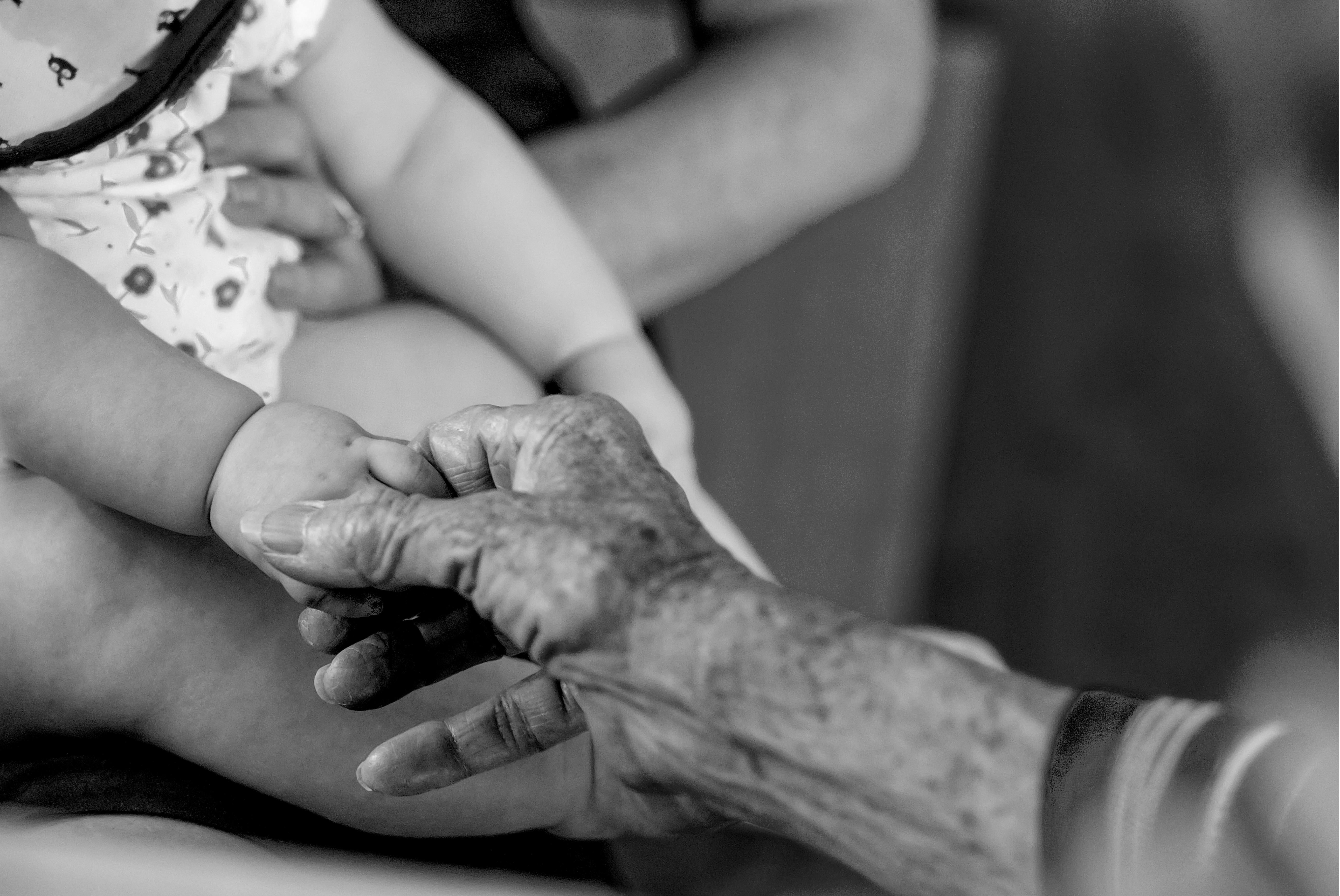A touching black and white image capturing a baby and senior adult holding hands, emphasizing generational connection.
