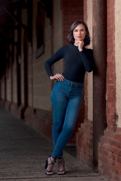 Free Confident woman in jeans and black top posing against a brick wall. Stock Photo