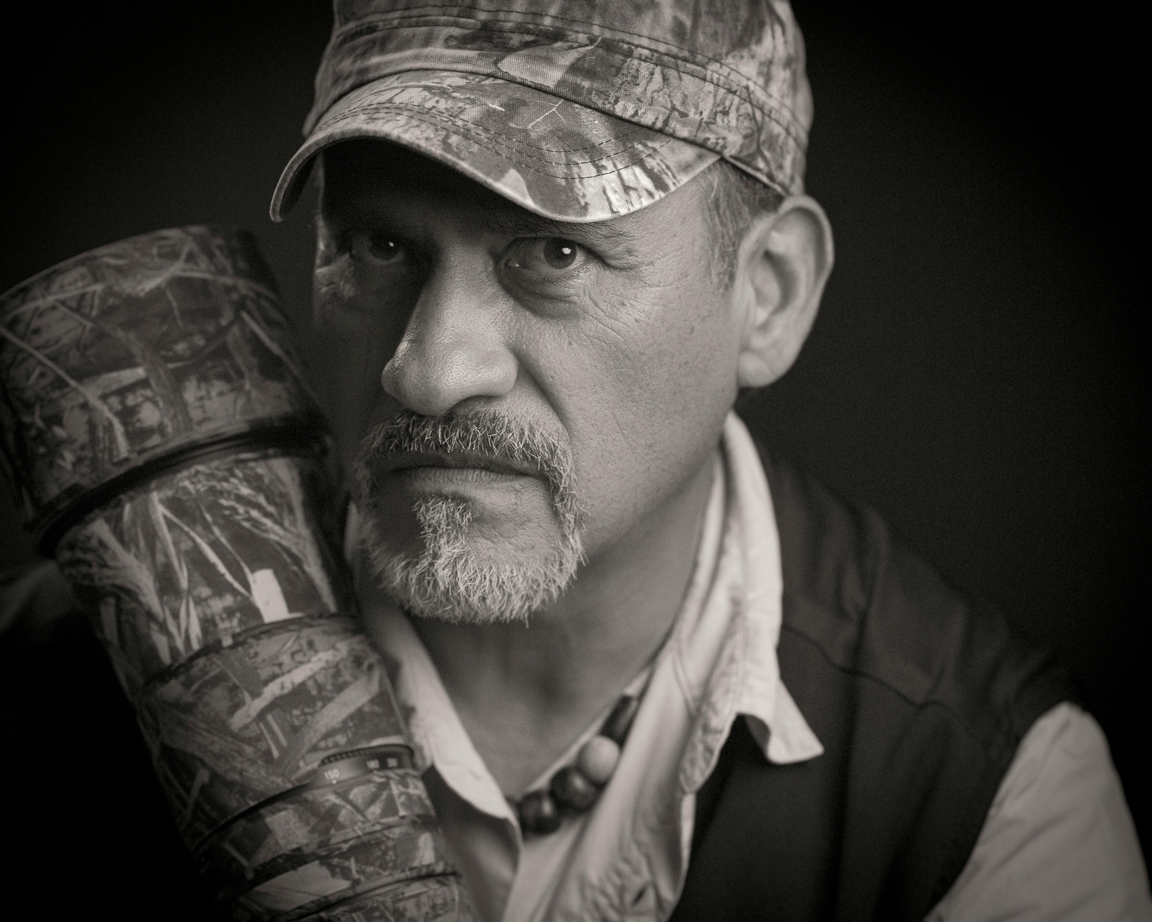 Black and white portrait of a serious elderly man wearing a camouflage hat and holding a patterned object.