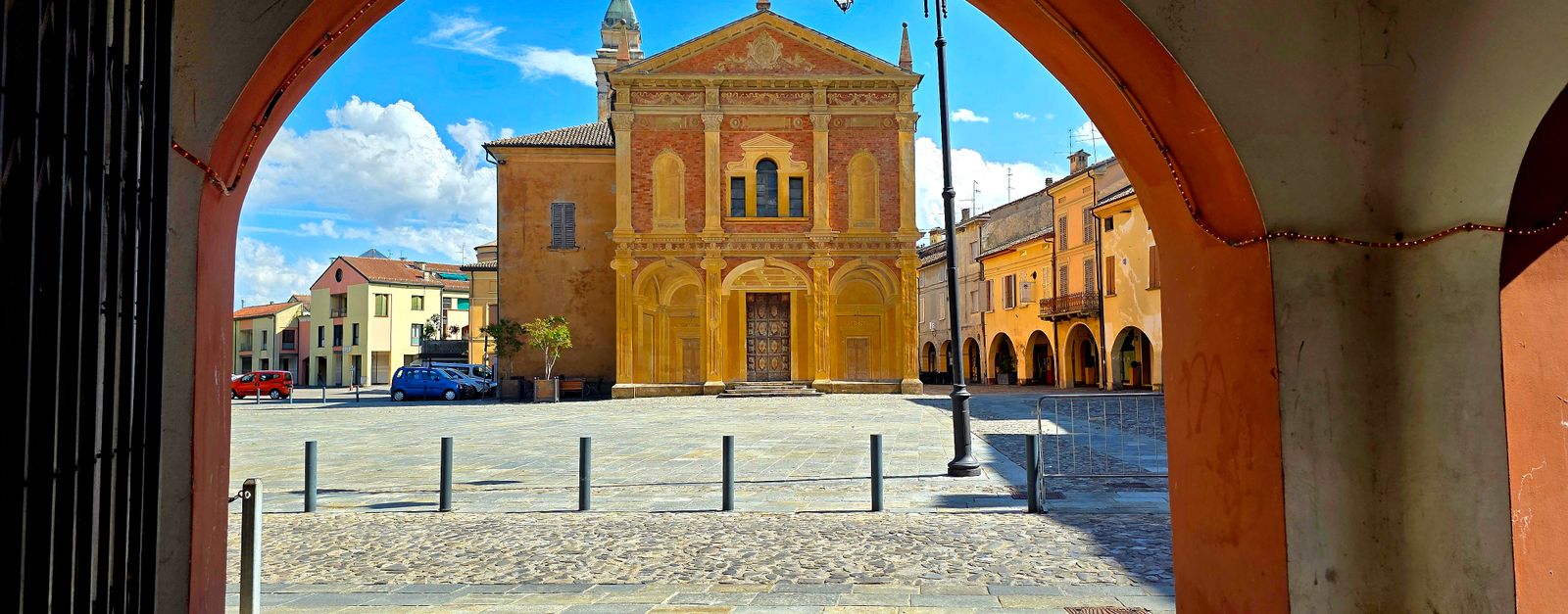 A charming Italian piazza viewed through a historic archway, featuring a classic church facade and blue sky.
