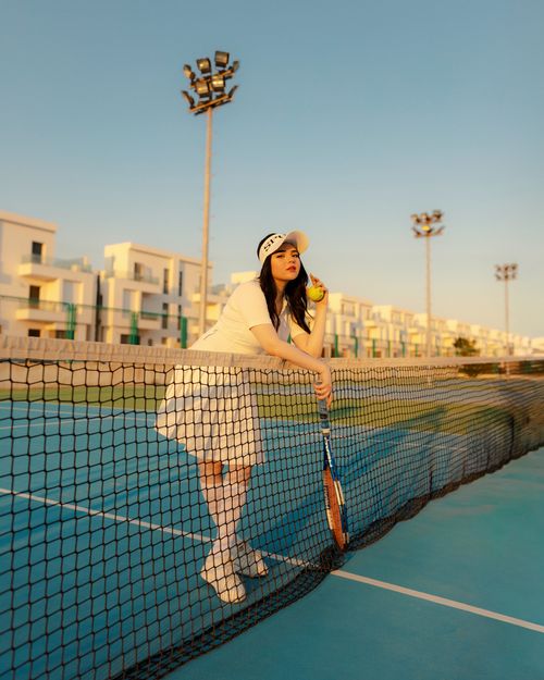 Free A female tennis player stands by the net on a sunlit court holding a tennis racket and ball. Stock Photo