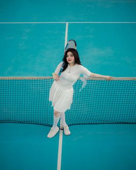 A young woman in white attire poses with a tennis racket mid-court, creating a dynamic sports scene.