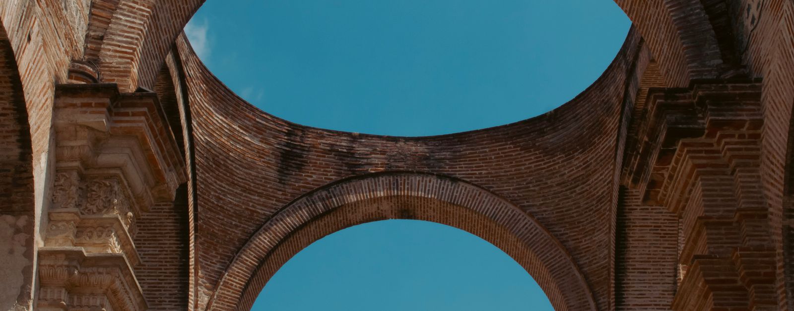 Elegant ancient brick arches of a historic ruin in Antígua, Guatemala, under a clear blue sky.
