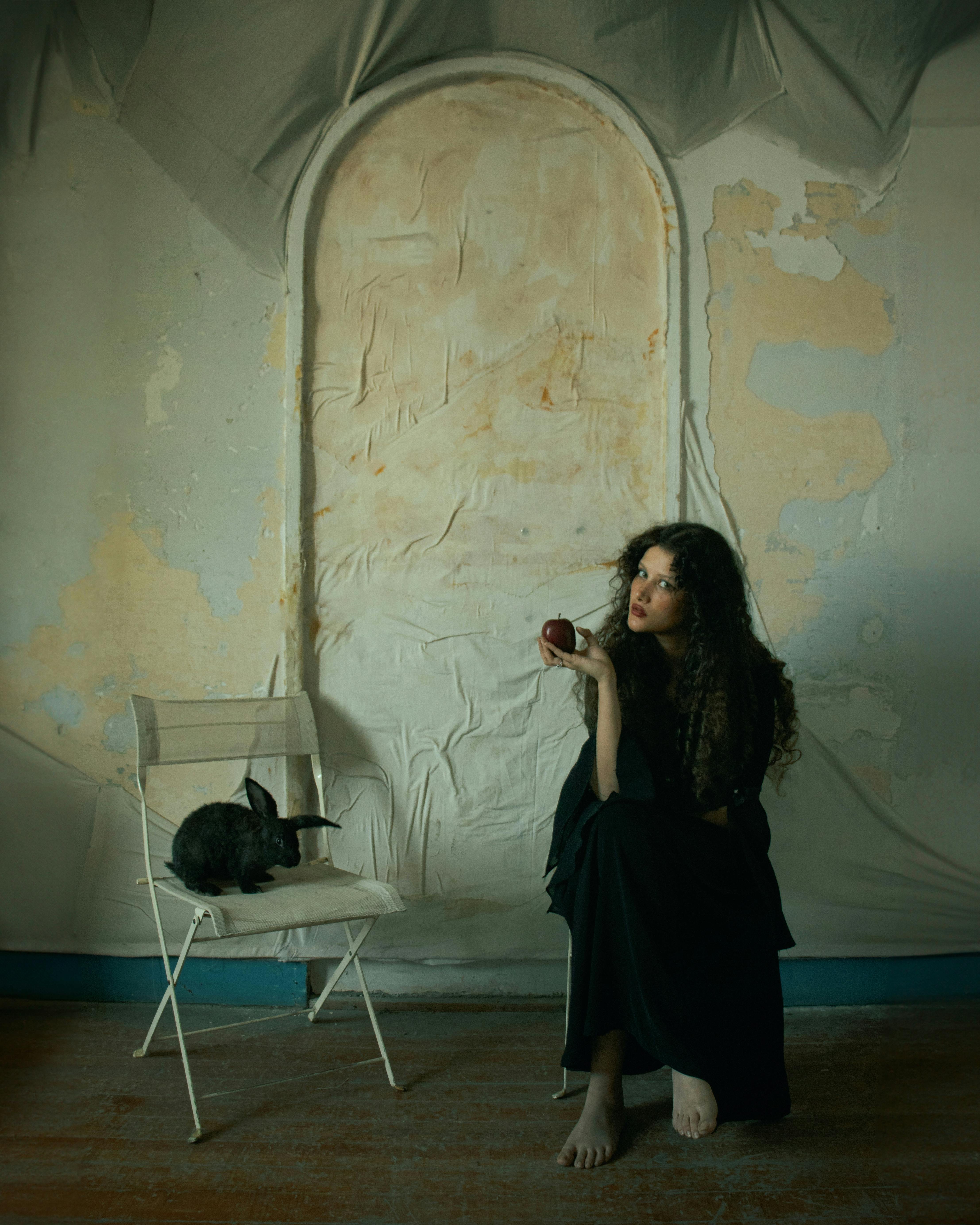Moody indoor portrait of a woman with a rabbit on a chair in an artistic setting.