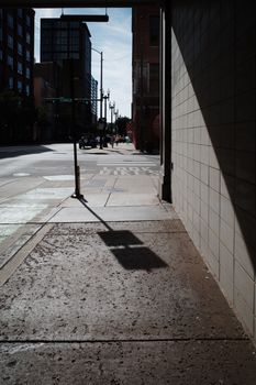 A shaded sidewalk leads towards a city street with visible high-rise buildings.