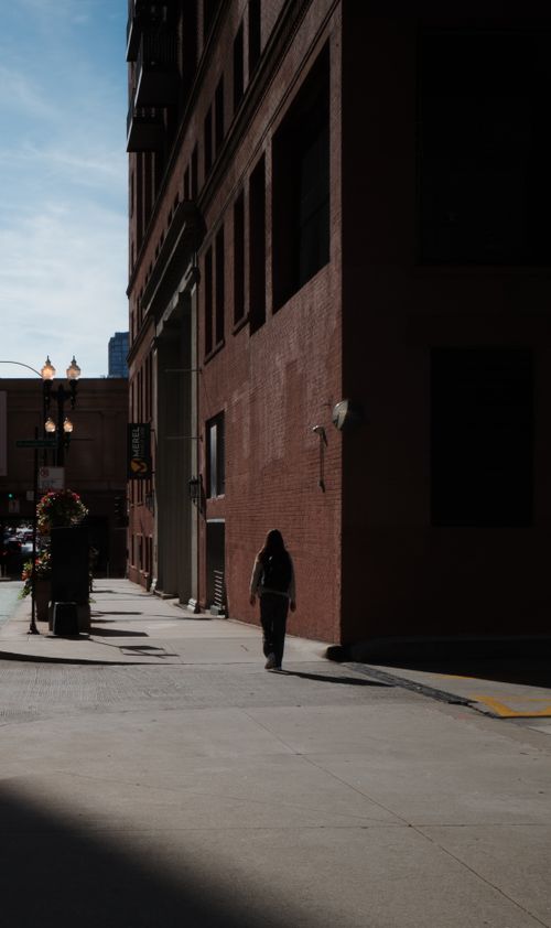 Free A lone figure walking down a sunlit urban alley, creating a dramatic silhouette effect. Stock Photo