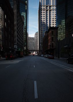 City street flanked by skyscrapers in downtown urban setting, under clear skies.