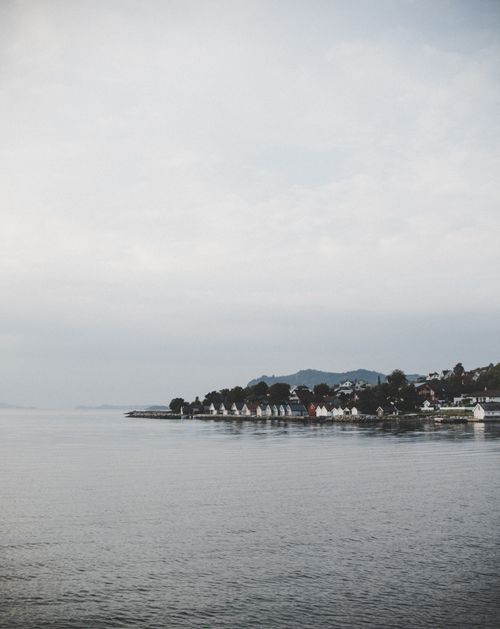 Free A serene view of a coastal village with houses lined along the water under a cloudy sky. Stock Photo
