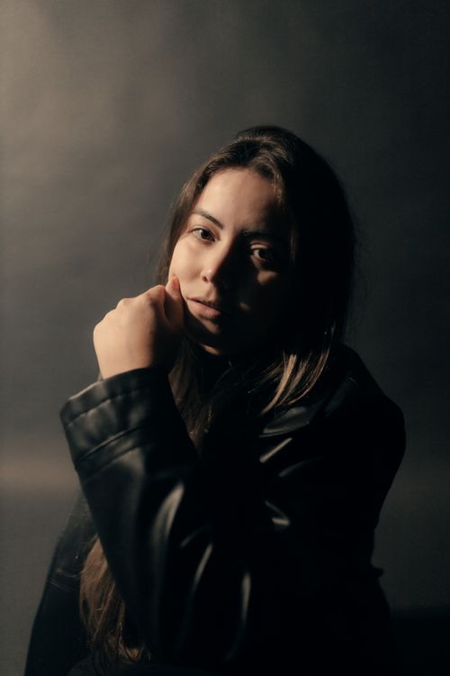 Free Moody portrait of a young woman in a leather jacket under dramatic lighting. Stock Photo
