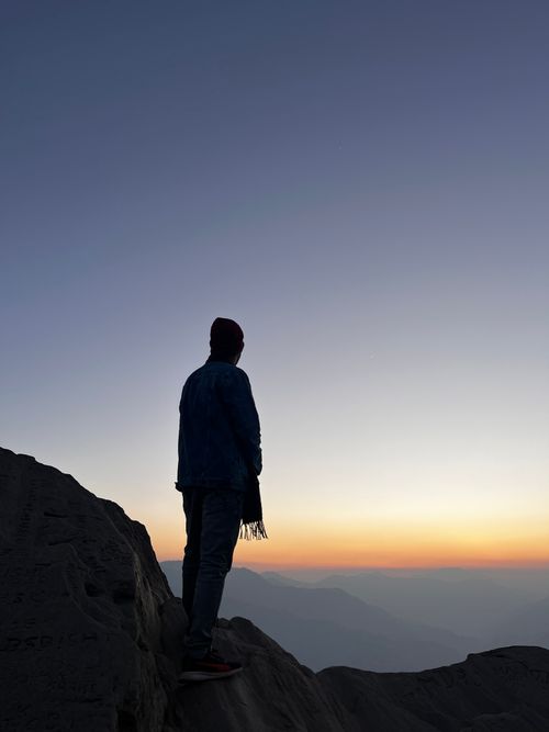 Free A person stands on a mountain edge at sunrise, contemplating the vast landscape. Stock Photo