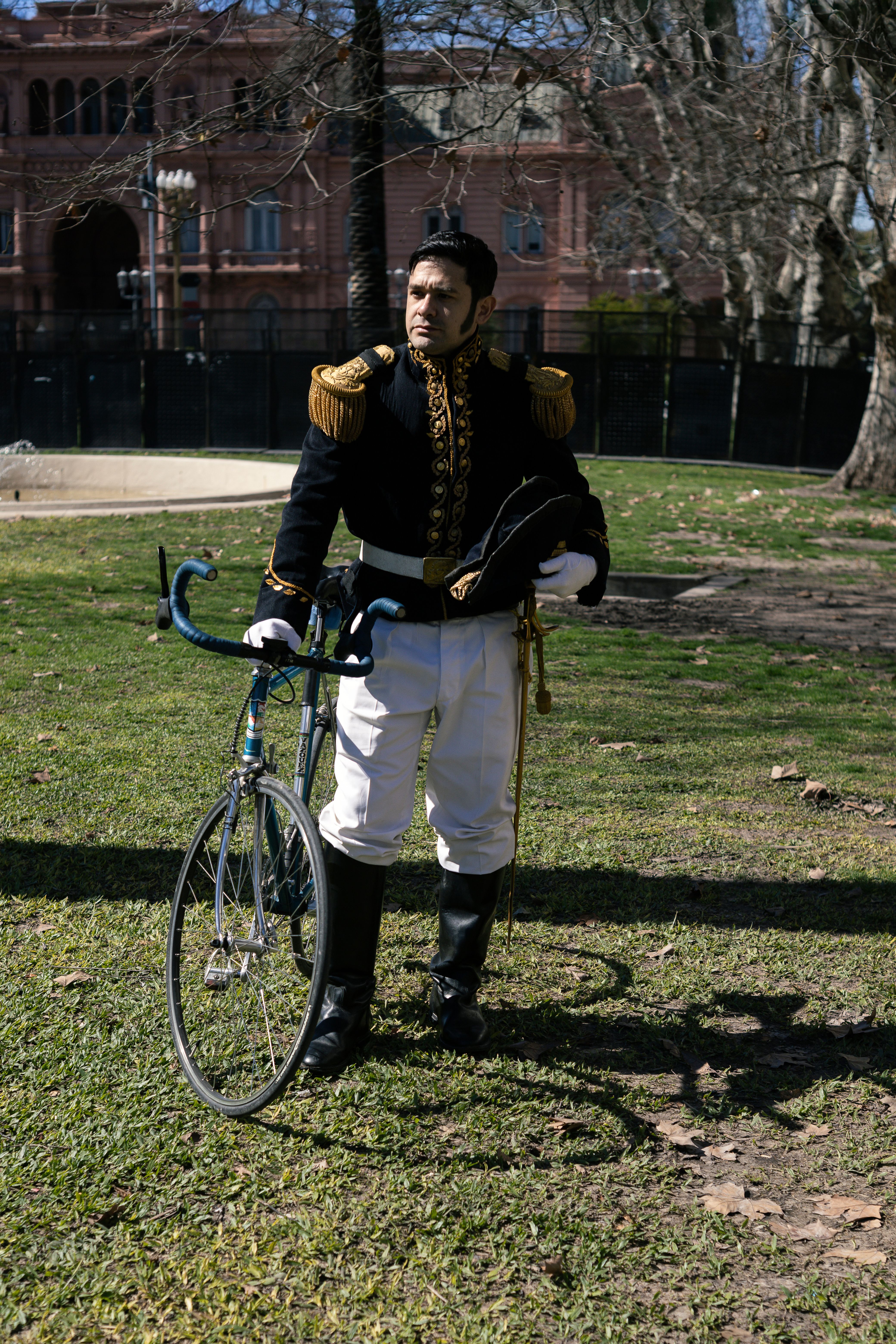 A man in a historical uniform stands with a bicycle in a park in Buenos Aires, Argentina.