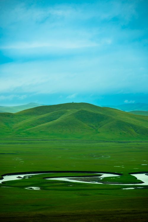 Free Serene landscape of rolling green hills beneath a bright blue sky with gentle clouds. Stock Photo