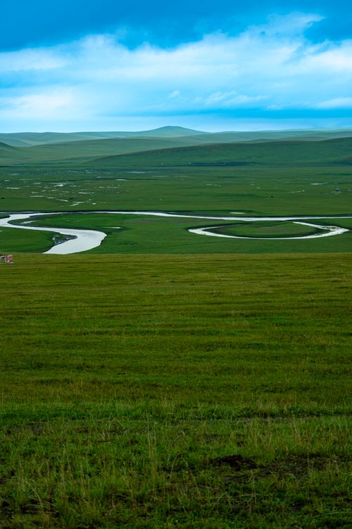Free Expansive grassland view featuring a meandering river under a vivid blue sky, ideal for nature themes. Stock Photo