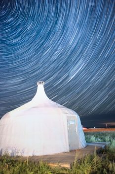 A stunning long exposure of star trails over a traditional yurt under the night sky.