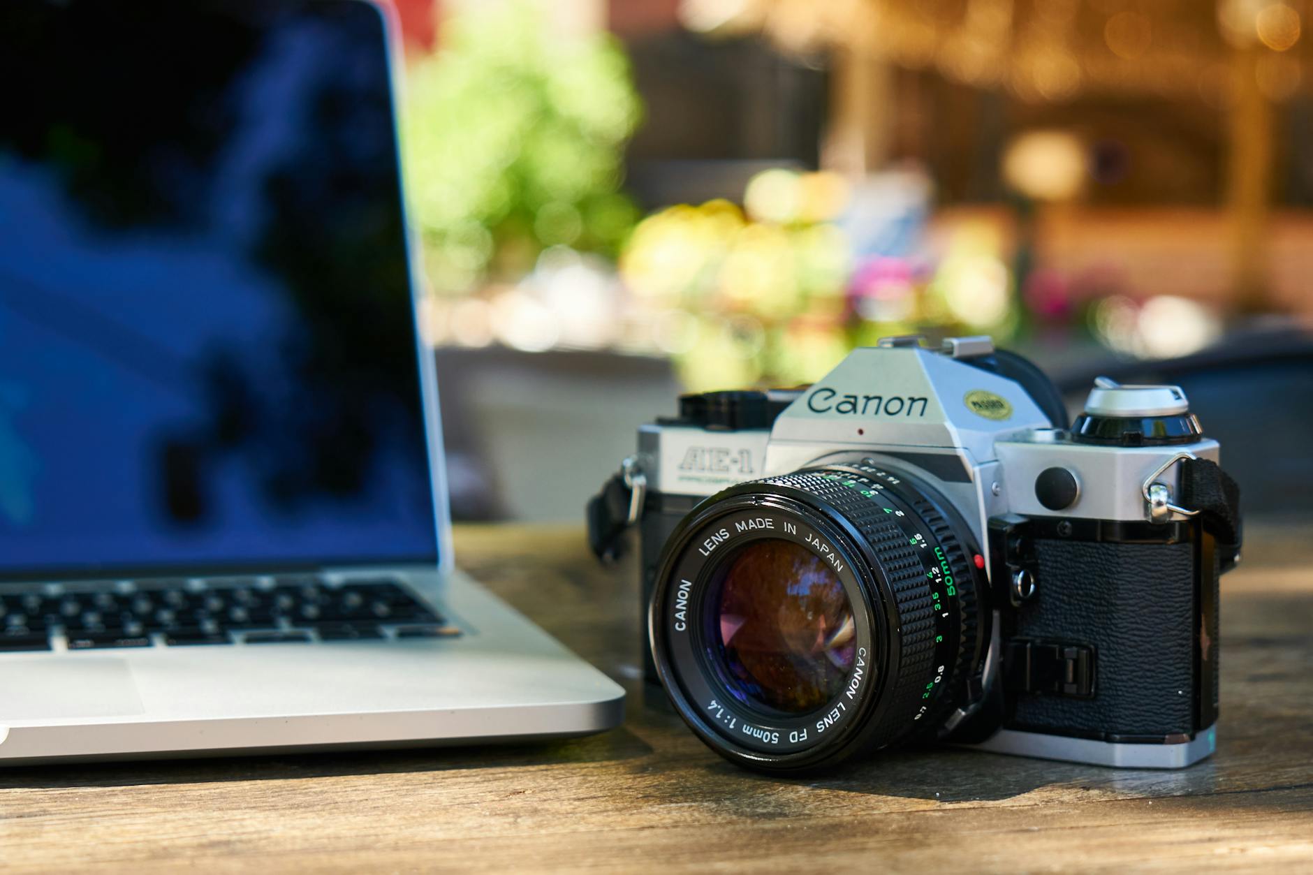A classic Canon film camera beside a laptop on a wooden table outdoors.