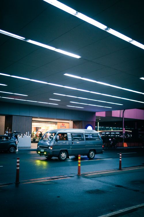 Free A vibrant urban evening scene featuring a van by a modern storefront under neon lights. Stock Photo