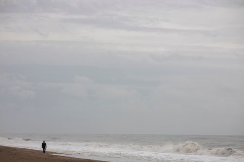 Free A lone figure walks along a stormy seaside with crashing waves under a cloudy sky. Stock Photo