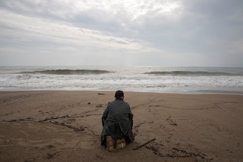 Person Wearing Gray Dress Shirt Sitting on Seashore