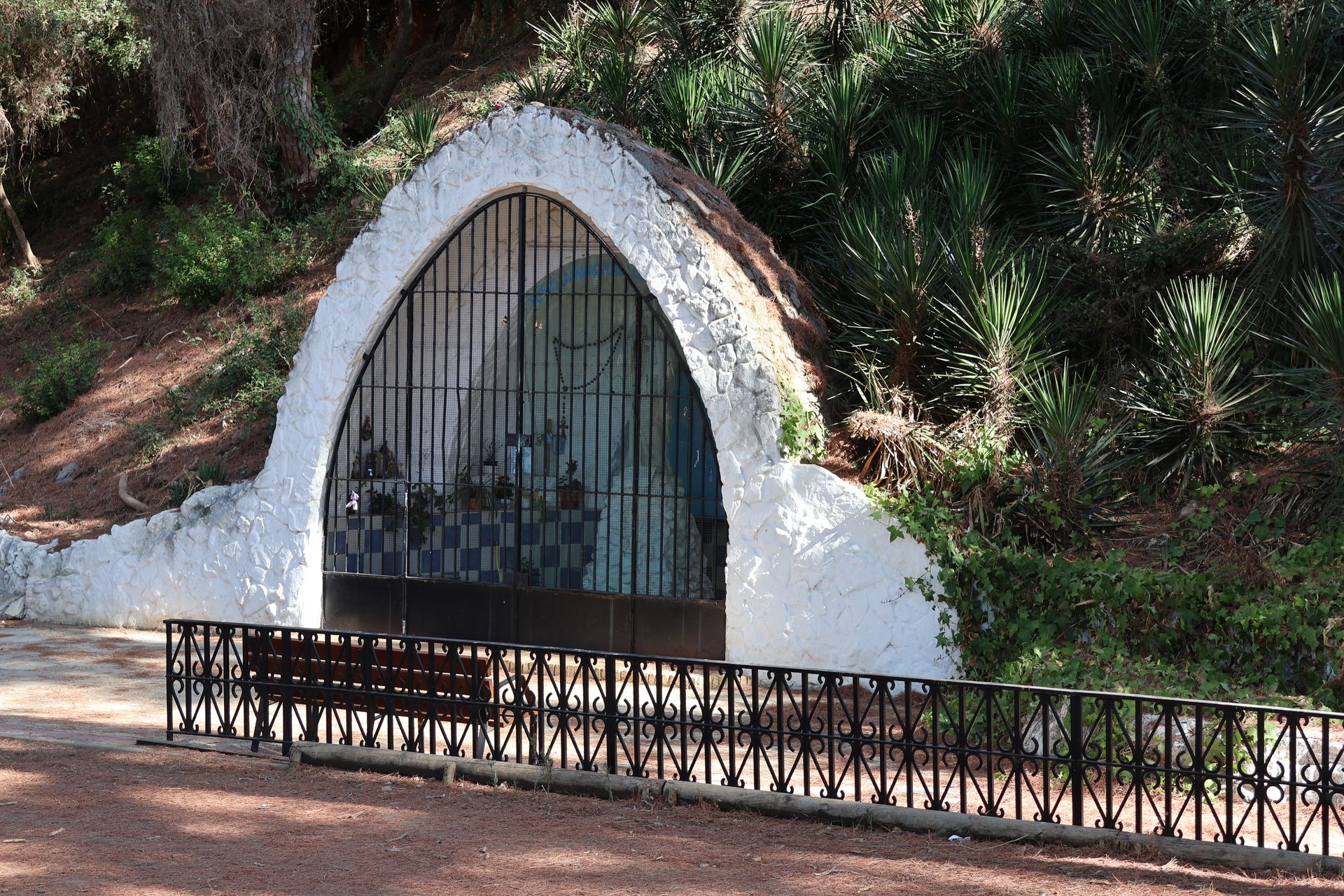 Serene grotto with religious artifacts nestled in a pinewood setting in Puerto Real, Andalucía.