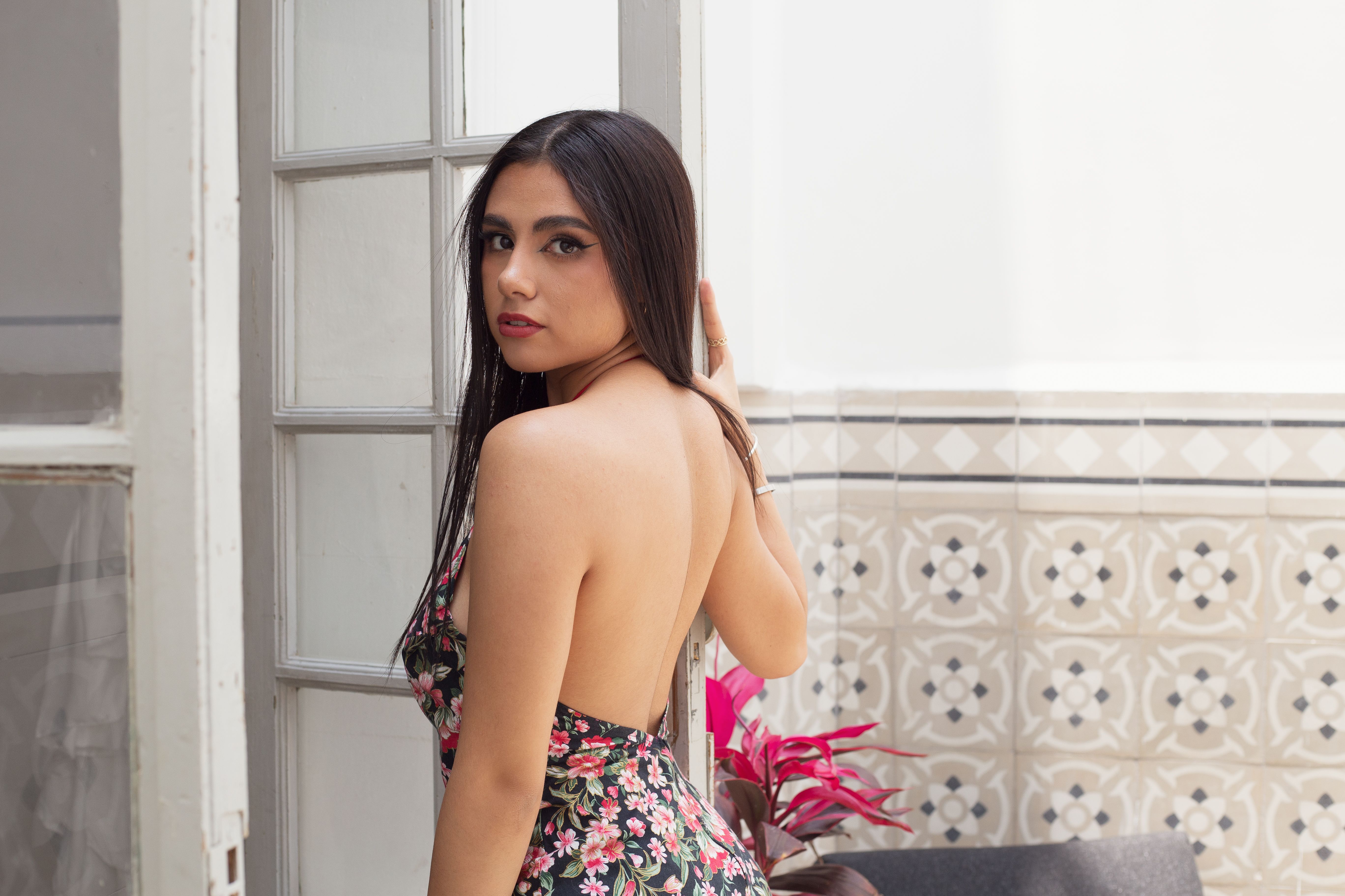 Elegant woman in a floral dress posing indoors with a bright background.