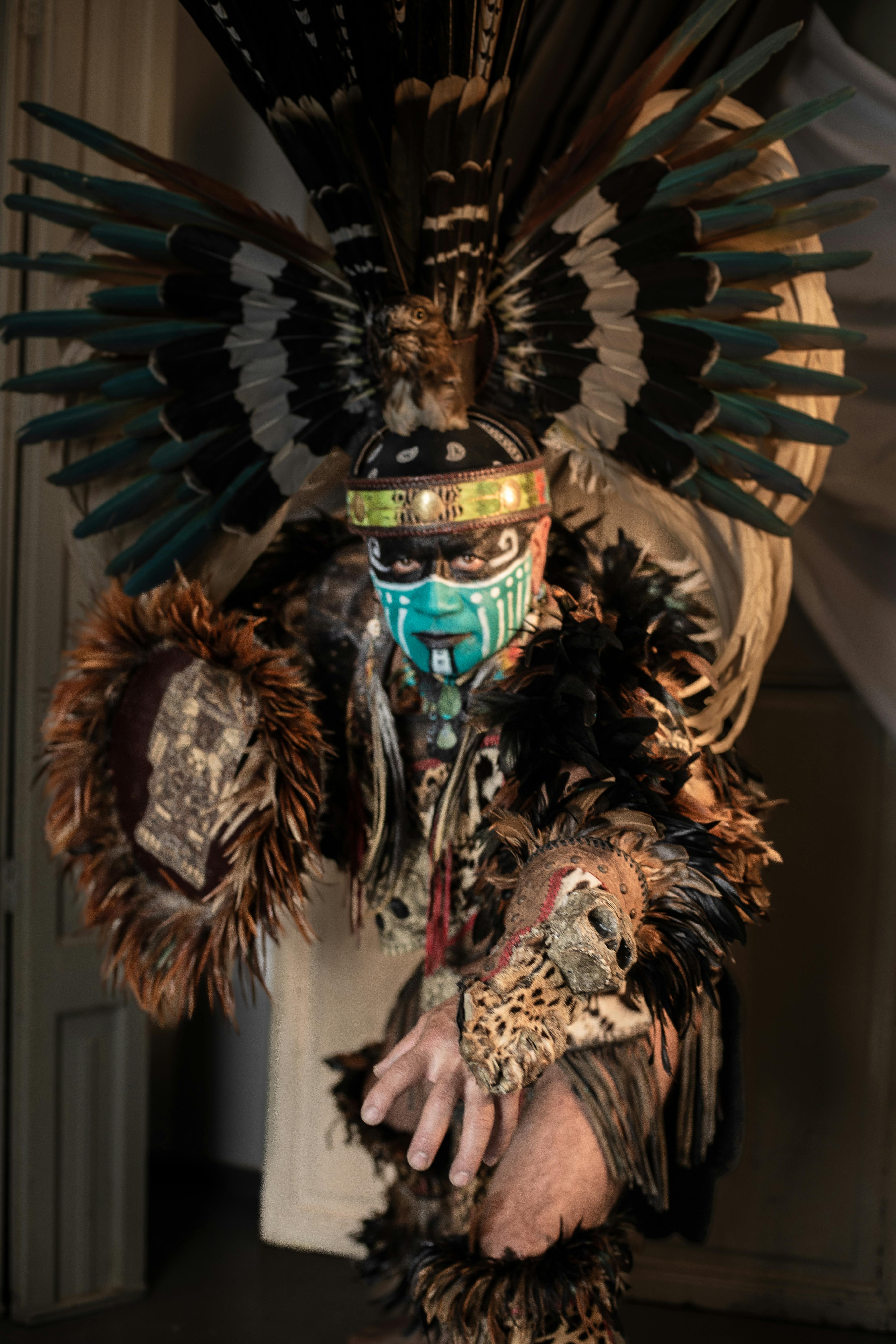 Aztec warrior in ornate feathered costume with face paint, embodying cultural heritage and tradition.