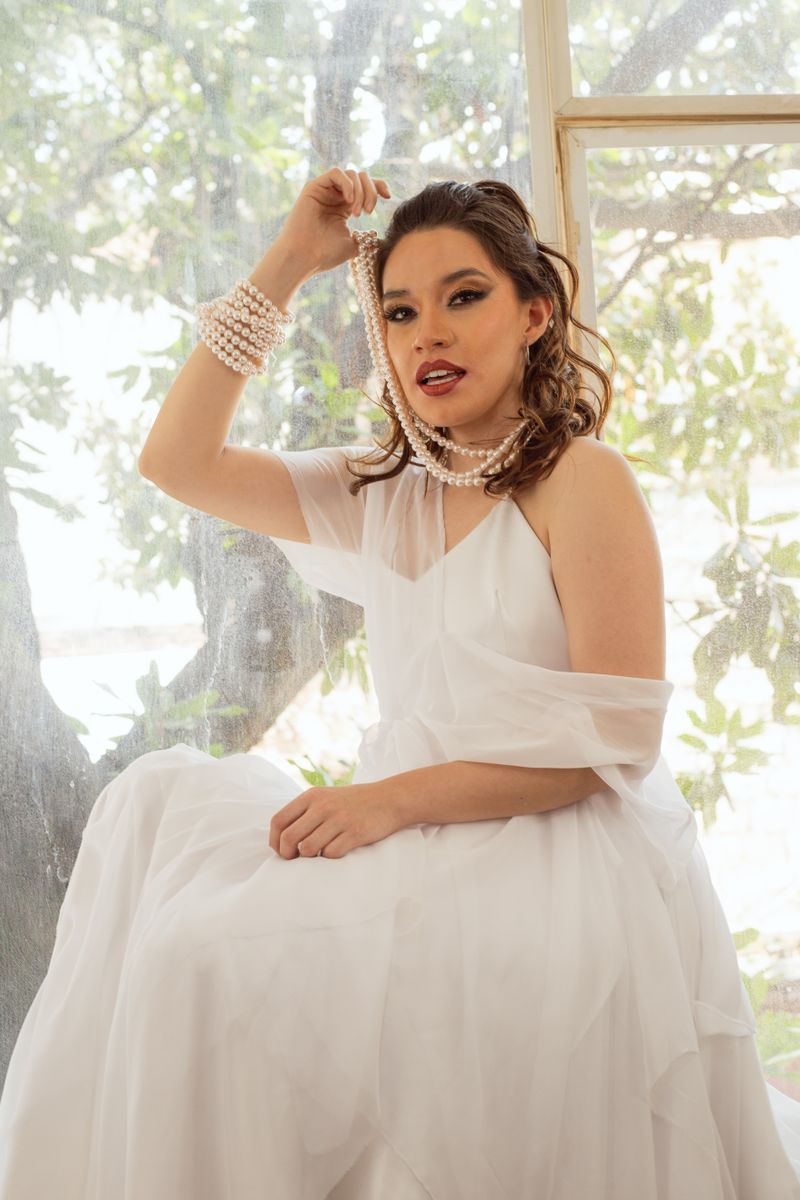 Elegant woman in white dress with pearls by window