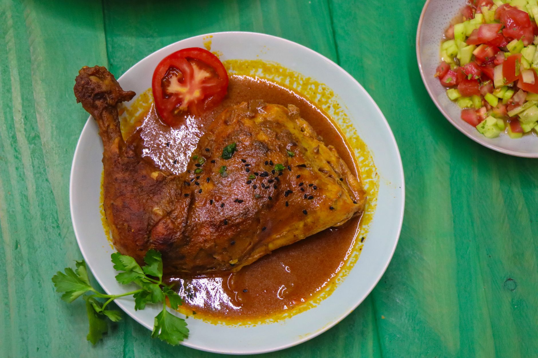 Golden-brown chicken thighs nestled in a rich, brick-red pepper and tomato sauce, served over a bed of fluffy bulgur pilaf and garnished with bright green parsley