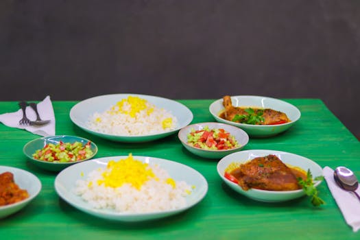 A vibrant Middle Eastern meal with rice, salad, and chicken served on a green table.
