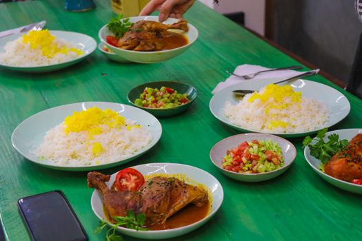A vibrant spread of rice, spiced chicken, and fresh salad served on a green table.