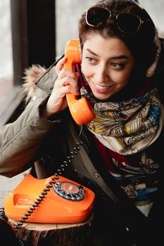 Woman wearing a scarf talks on a vintage orange rotary phone, adding a retro feel.