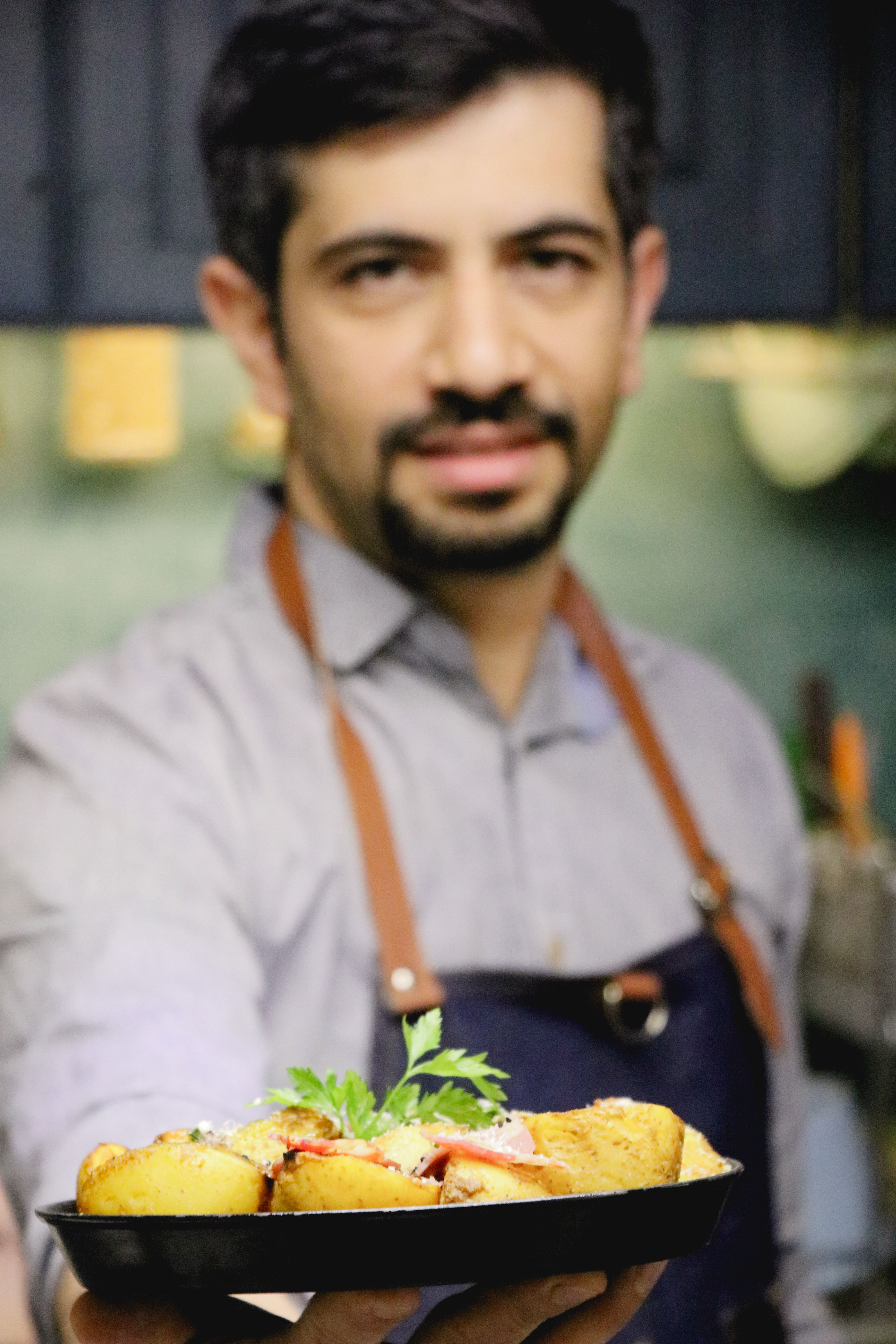 Smiling chef proudly displaying a gourmet dish in a modern kitchen setting.
