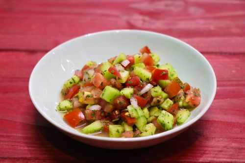 Free A vibrant cucumber and tomato salad in a white bowl, set on a red wooden table. Stock Photo