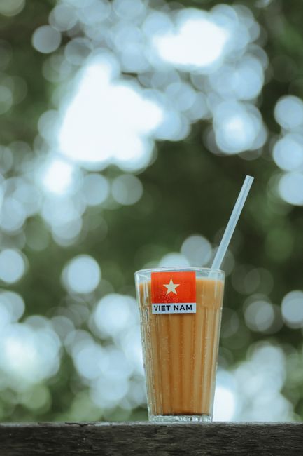 Cách Nấu Sữa Macca Úc Thơm Béo Mịn, Không Bị Lợn Cợn 2 Vietnamese iced coffee with straw and Vietnam flag label, in front of a blurred bokeh background.
