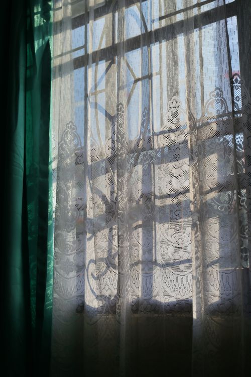Free Soft sunlight filters through ornate lace curtains indoors, casting delicate patterns. Stock Photo