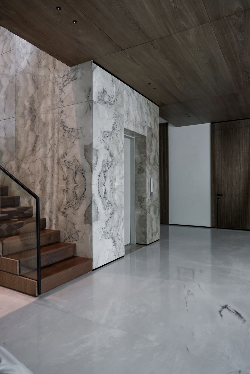 Sleek modern interior featuring marble walls and wooden staircase, exuding luxury.