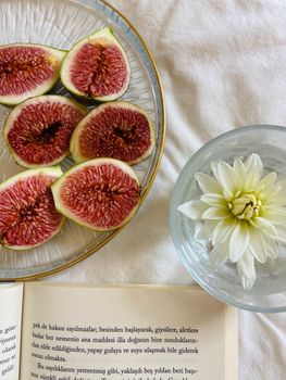 Sliced figs with a white flower in water, and an open book on a white surface.