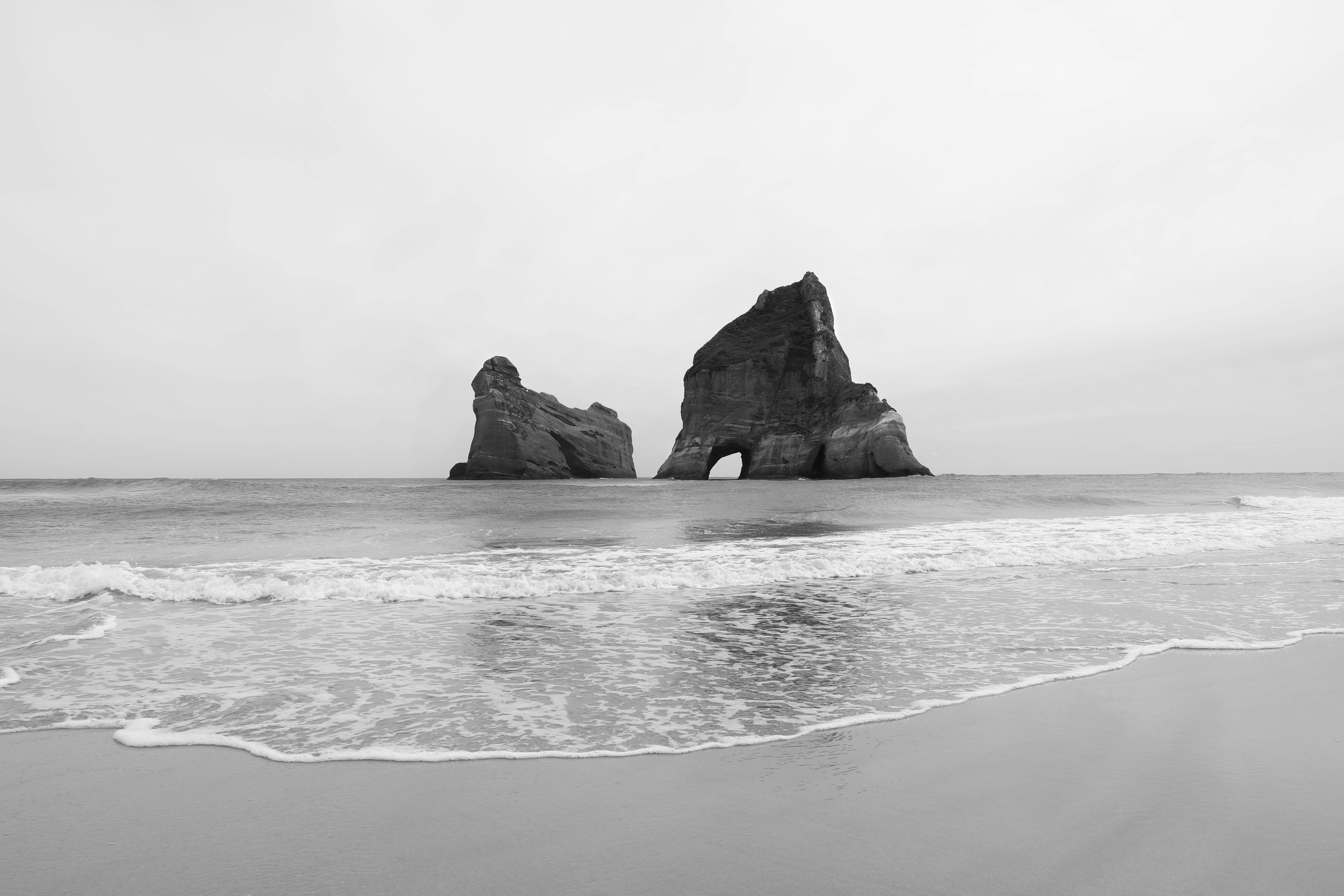 Monochrome view of iconic rock arches at Wharariki Beach, New Zealand's scenic coastline.